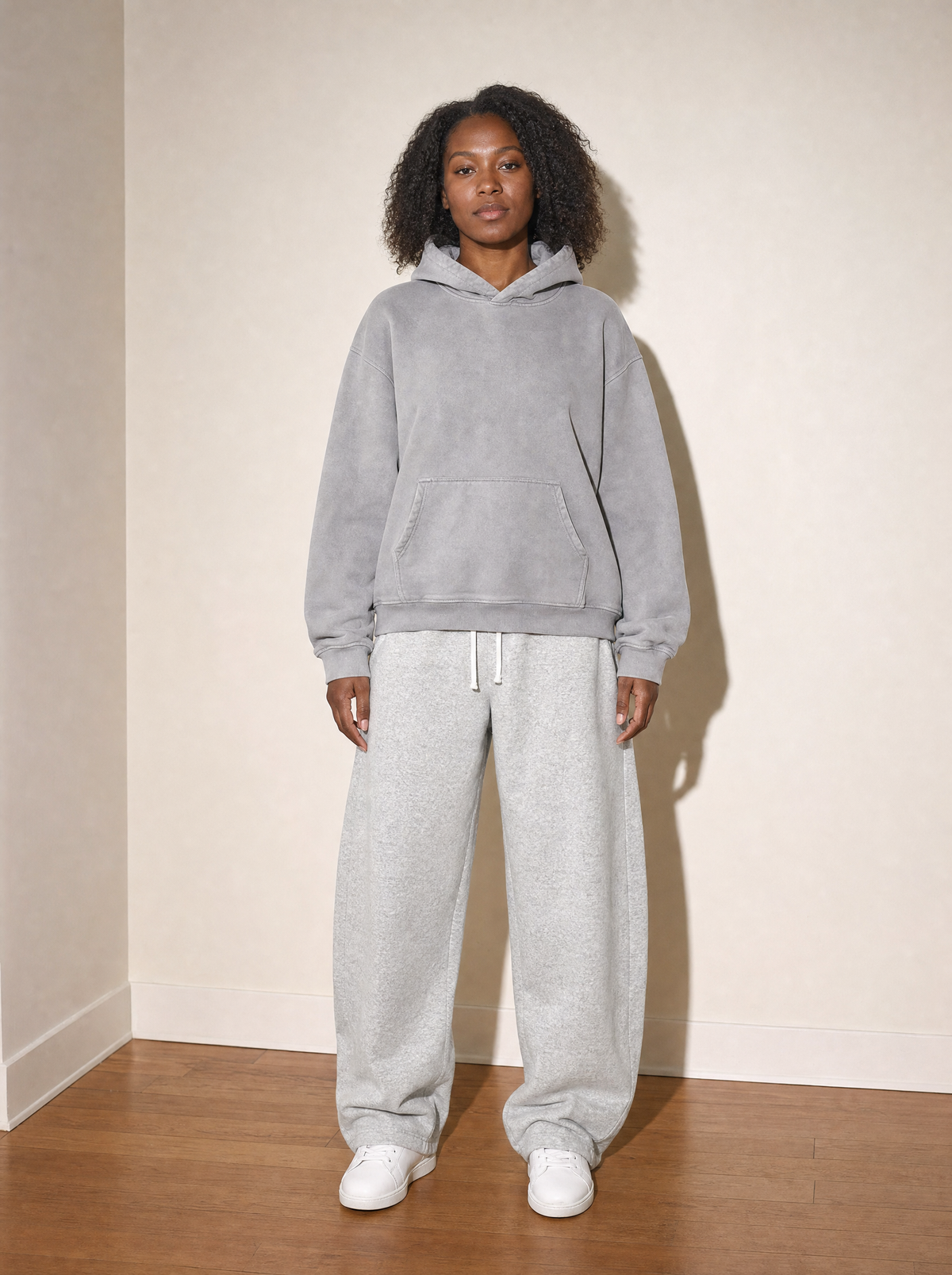 Home & Away Set - Gray, front view, worn against the apartment wall: the 400 gsm hoodie with the 350 gsm barrel sweatpant
