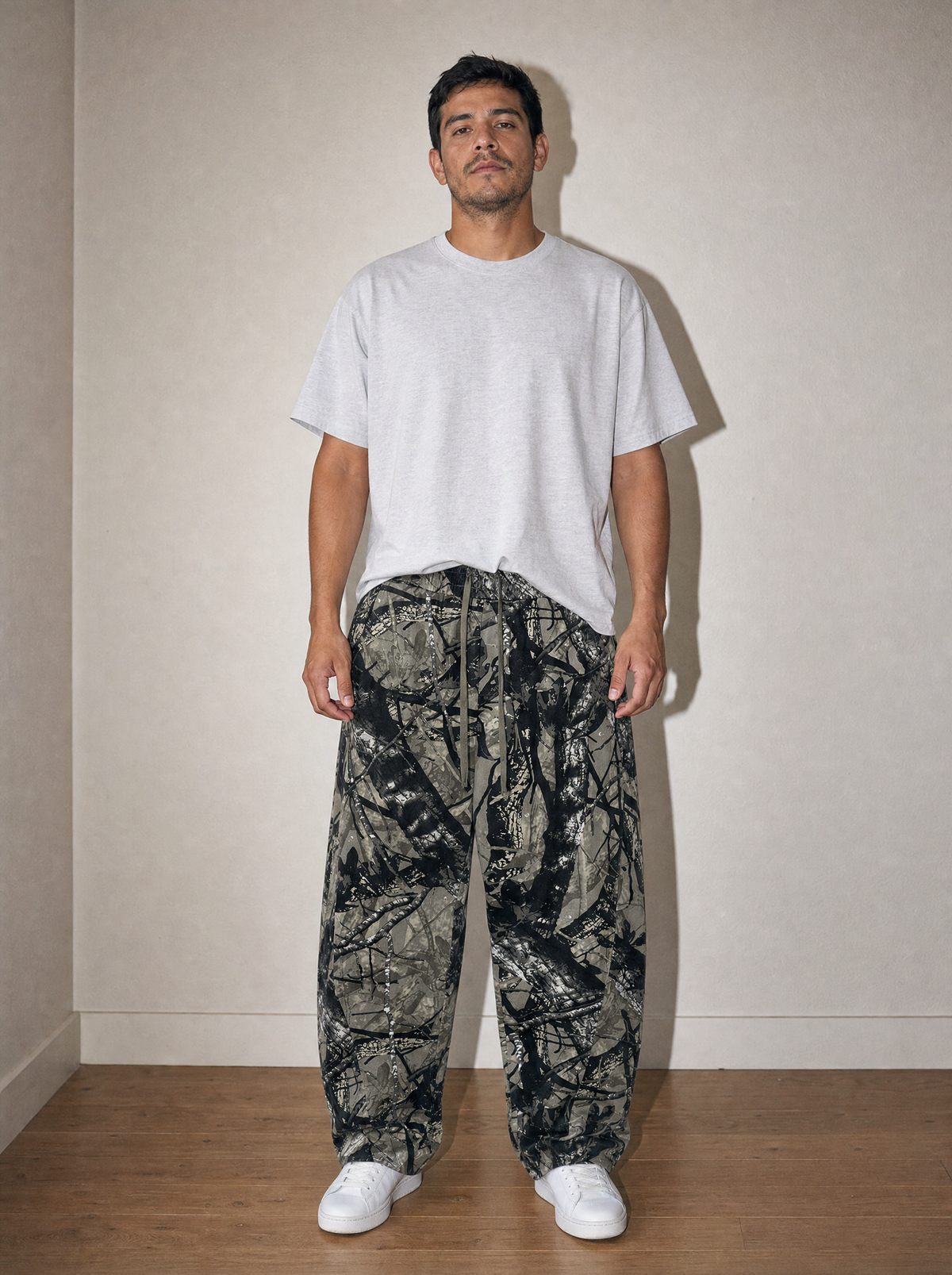 Tree Camo Barrel Pant in Gray Tree Camo, front view, worn against the apartment wall: 340 gsm woven cotton in an all-over tree camo